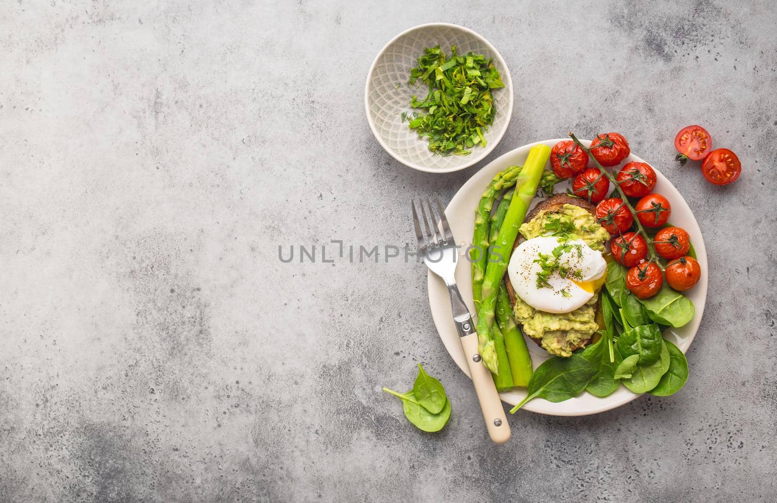 Healthy vegetarian meal plate. Toast, avocado, poached egg, asparagus, baked tomatoes, spinach. Stone background. Space for text. Vegetarian breakfast plate. Diet. Organic clean healthy food. Top view