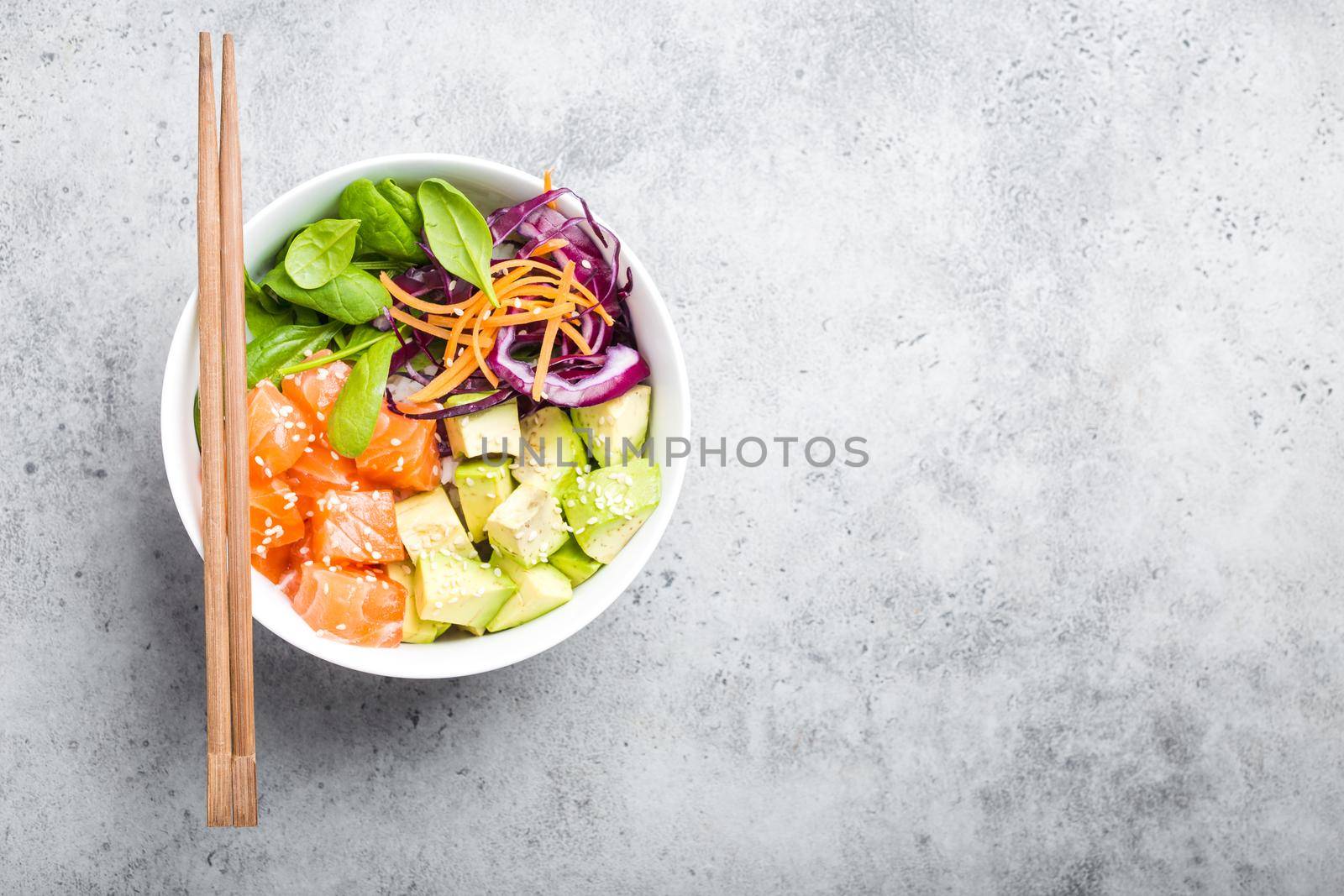Top view of poke bowl with fresh raw salmon and vegetables, space for text. Traditional Hawaiian dish on rustic stone background. Healthy and clean eating concept. Poke with slices of fish, copy space