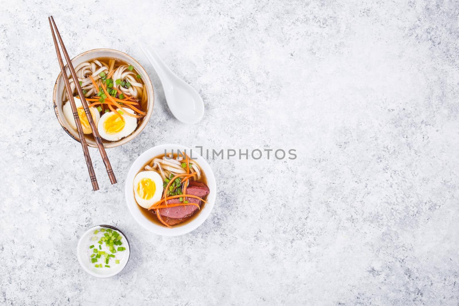 Bowls with Japanese soup ramen, chopsticks, white concrete rustic background. Traditional Asian soup with noodles, meat, eggs. Asian food. Japanese ramen for dinner. Space for text. Ramen, top view