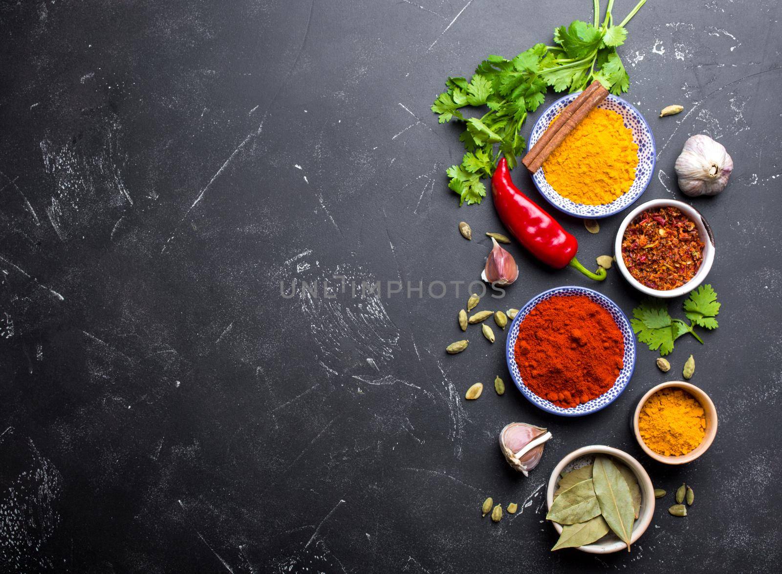 Indian food cooking background. Traditional Indian spices and ingredients. Curry, turmeric, cardamom, garlic, pepper, fresh cilantro, cinnamon. Preparing exotic meal. Top view, space for text