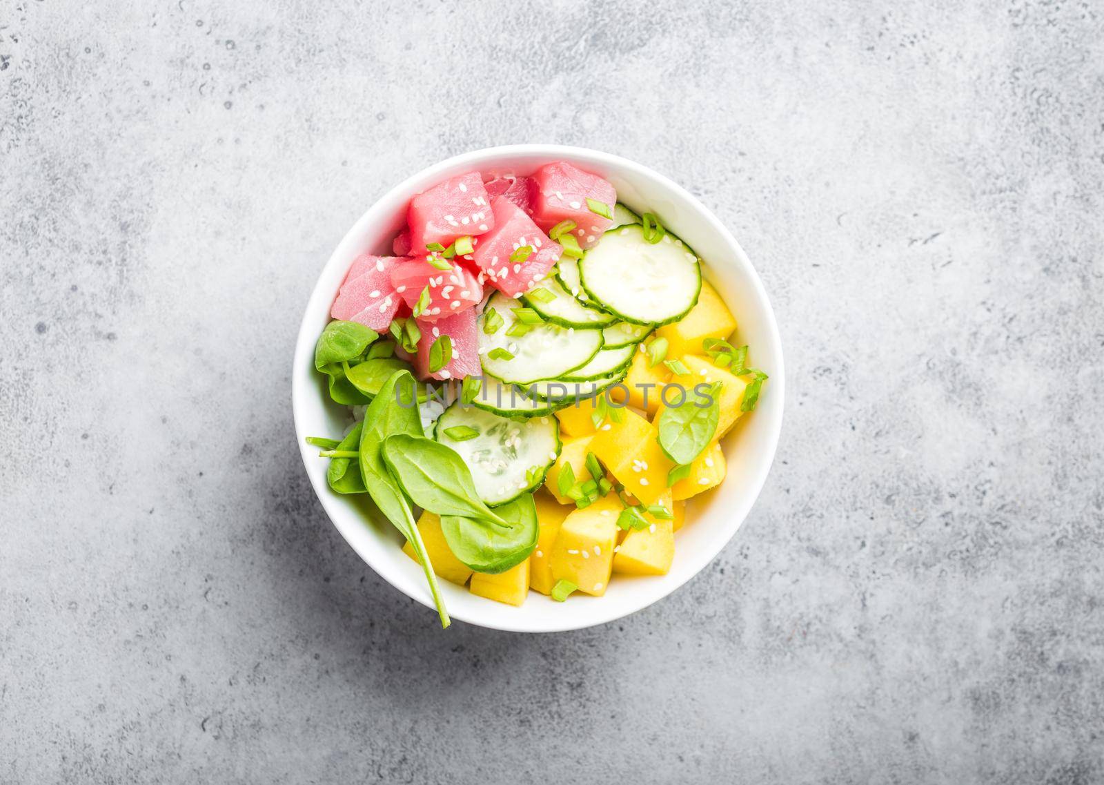 Top view of poke bowl with fresh raw tuna, mango, rice, spinach, cucumber. Traditional Hawaiian dish on rustic stone background. Healthy and clean eating concept. Poke with slices of raw fish