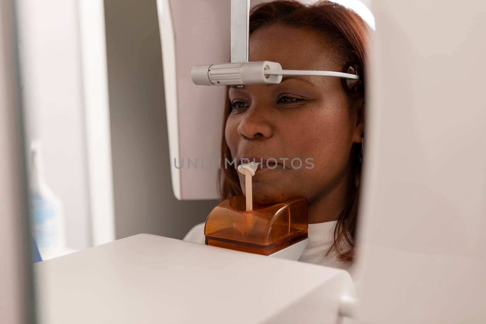 A black woman patient standing at the x-rays machine during the treatment at the dental clinic