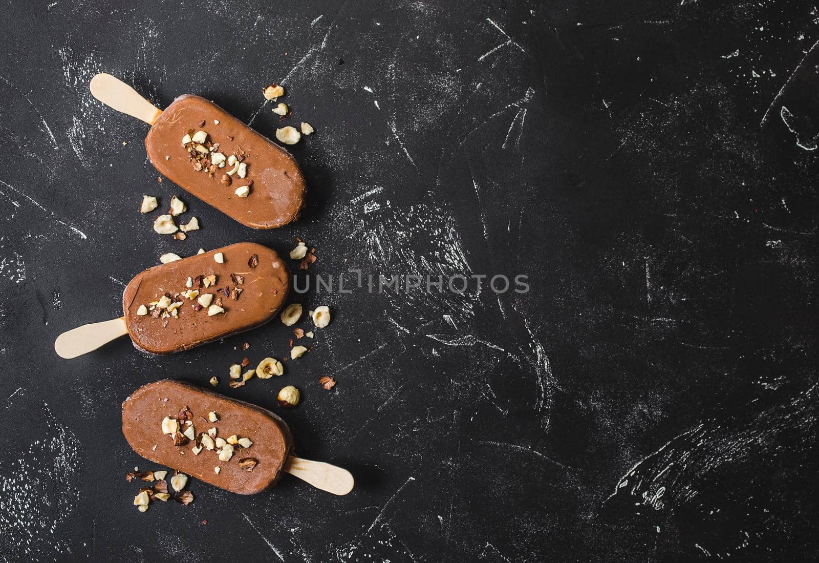 Milk chocolate popsicles with hazelnuts. Ice cream popsicles covered with chocolate, sticks, black stone marble background. Space for text. Top view. Chocolate ice cream bars, nuts. Ice cream dessert