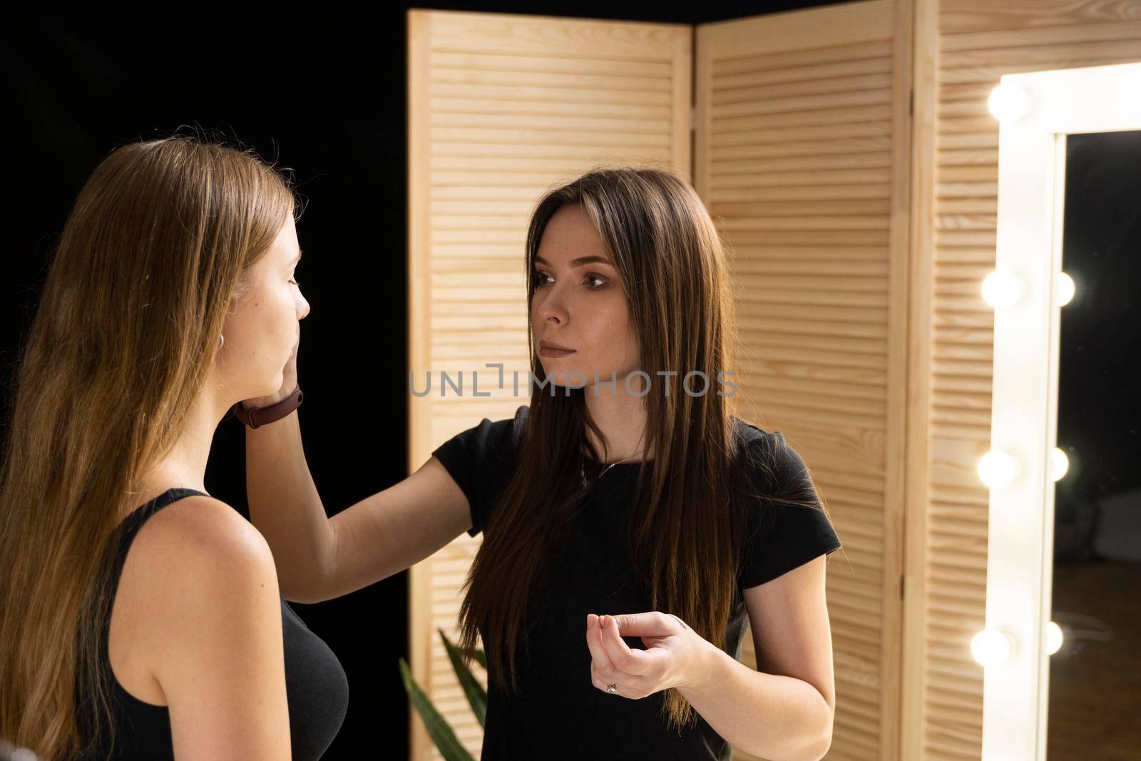 Makeup artist applying liquid tonal foundation on the face of the woman. Professional make up in a visage studio