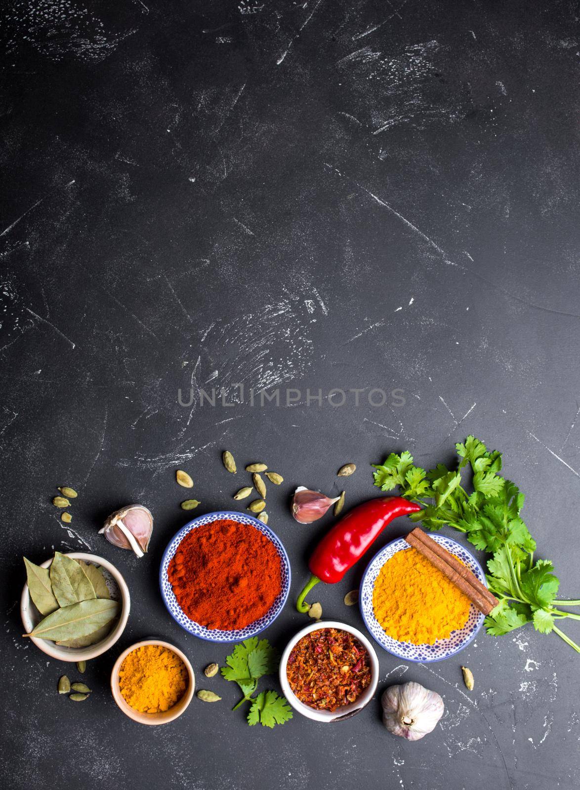 Indian food cooking background. Traditional Indian spices and ingredients. Curry, turmeric, cardamom, garlic, pepper, fresh cilantro, cinnamon. Preparing exotic meal. Top view, space for text