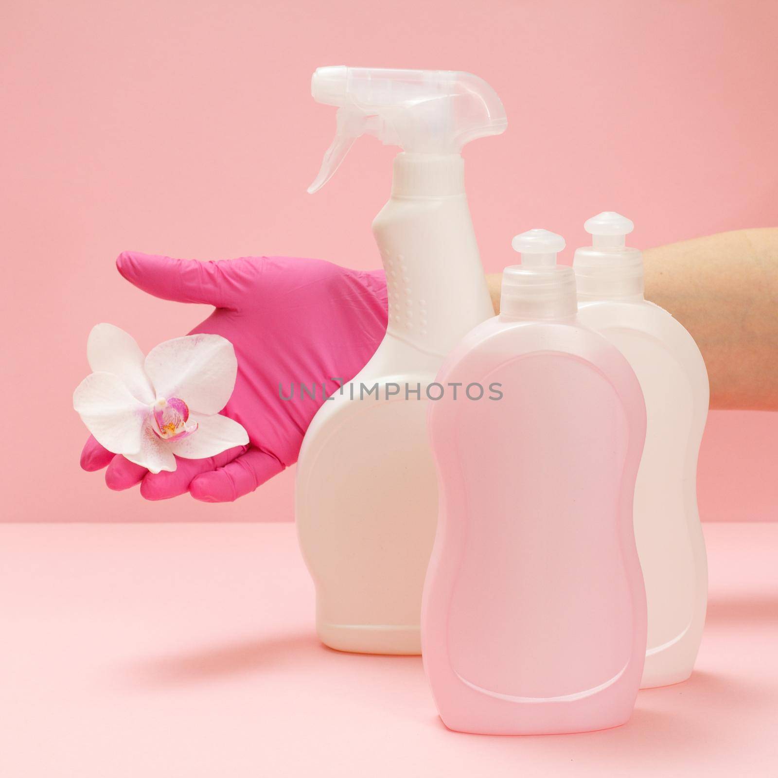 Bottles of washing liquid and a hand with a orchid flower on a pink background. by mvg6894