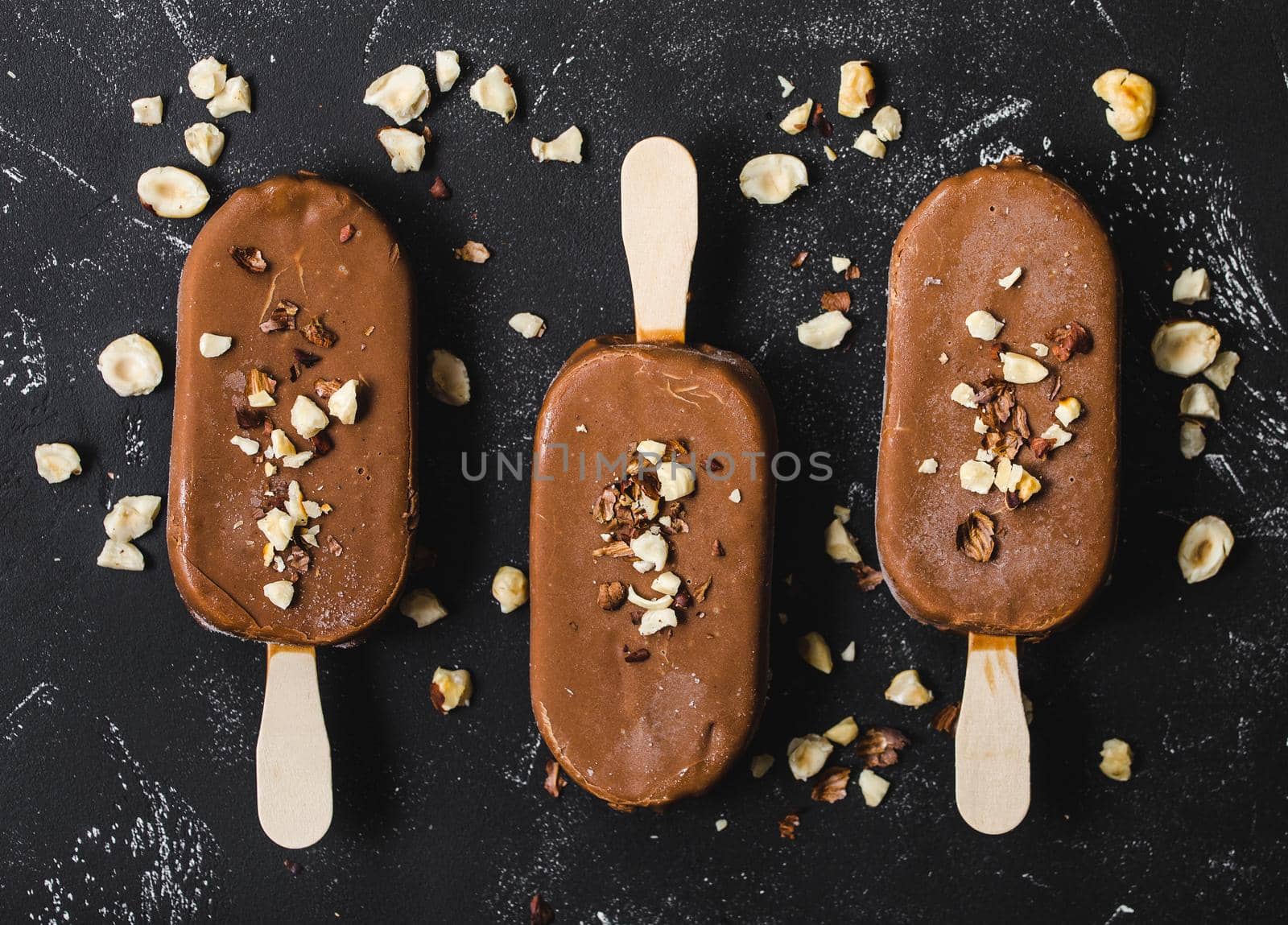 Milk chocolate popsicles with hazelnuts. Close-up. Ice cream popsicles covered with chocolate, sticks, black stone background. Top view. Chocolate ice cream bars, nuts. Dessert. Ice cream concept