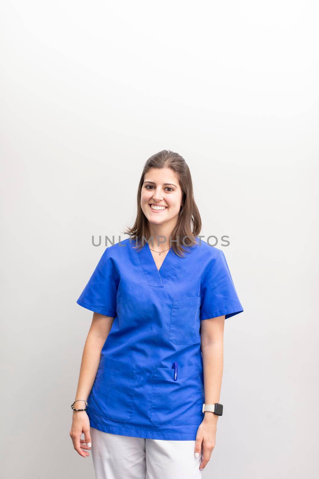 An american shot portrait of a caucasian woman dentist, smiling with joy and looking at camera wearing blue uniform at the dental clinic