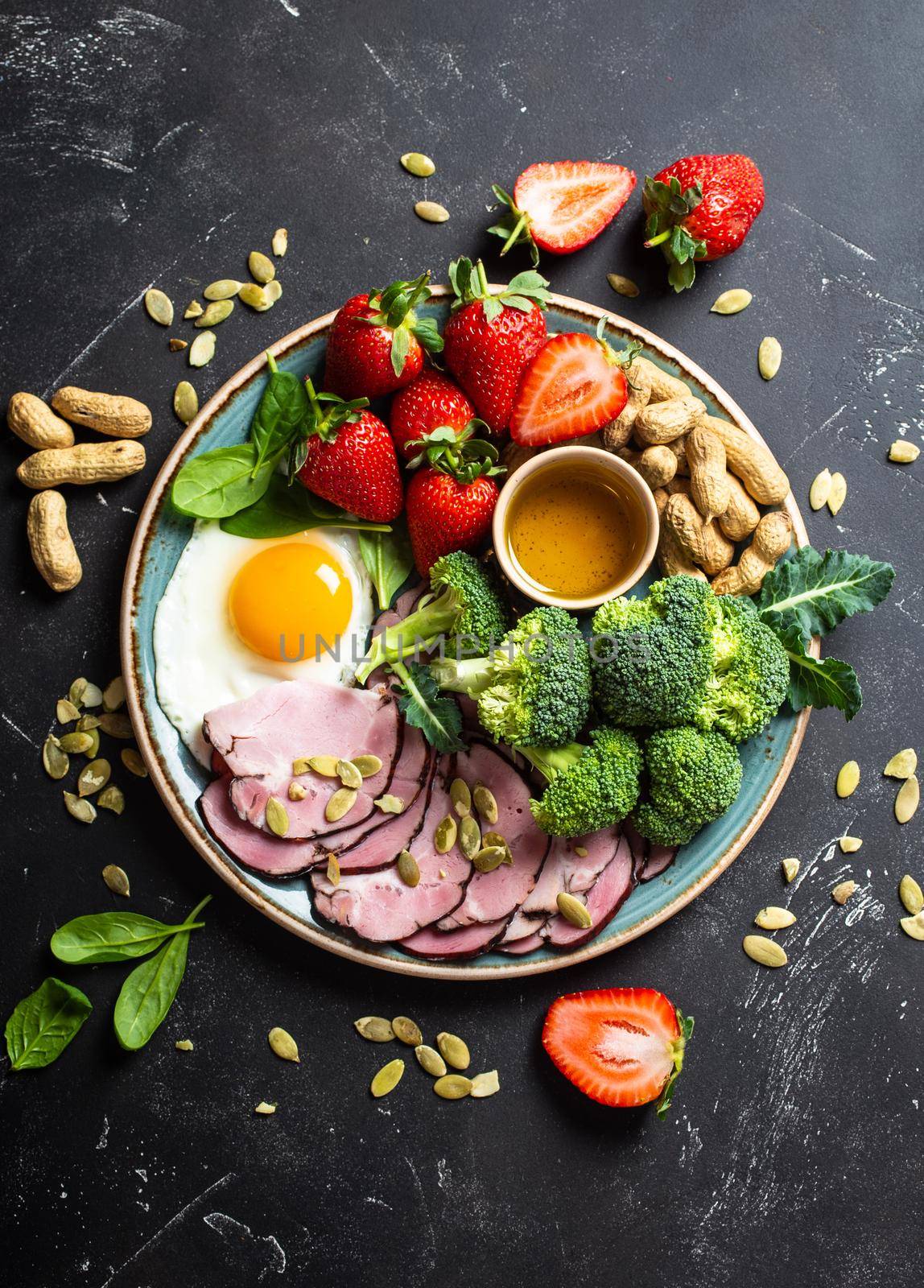 Ketogenic low carbs diet concept, top view. Plate on stone black background with keto foods: egg, meat, olive oil, broccoli, berries, nuts, seeds, spinach. Healthy fats, clean eating for weight lossdietdi