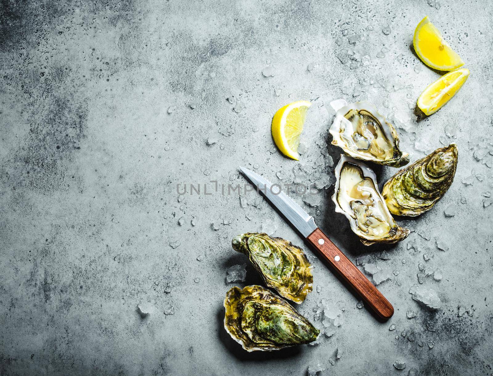 Fresh oysters on ice, knife, lemon wedges. Rustic stone background. Opened fresh raw oysters. Top view. Copy space. Oyster bar. Seafood. Oysters concept. Party food. Space for text. From above