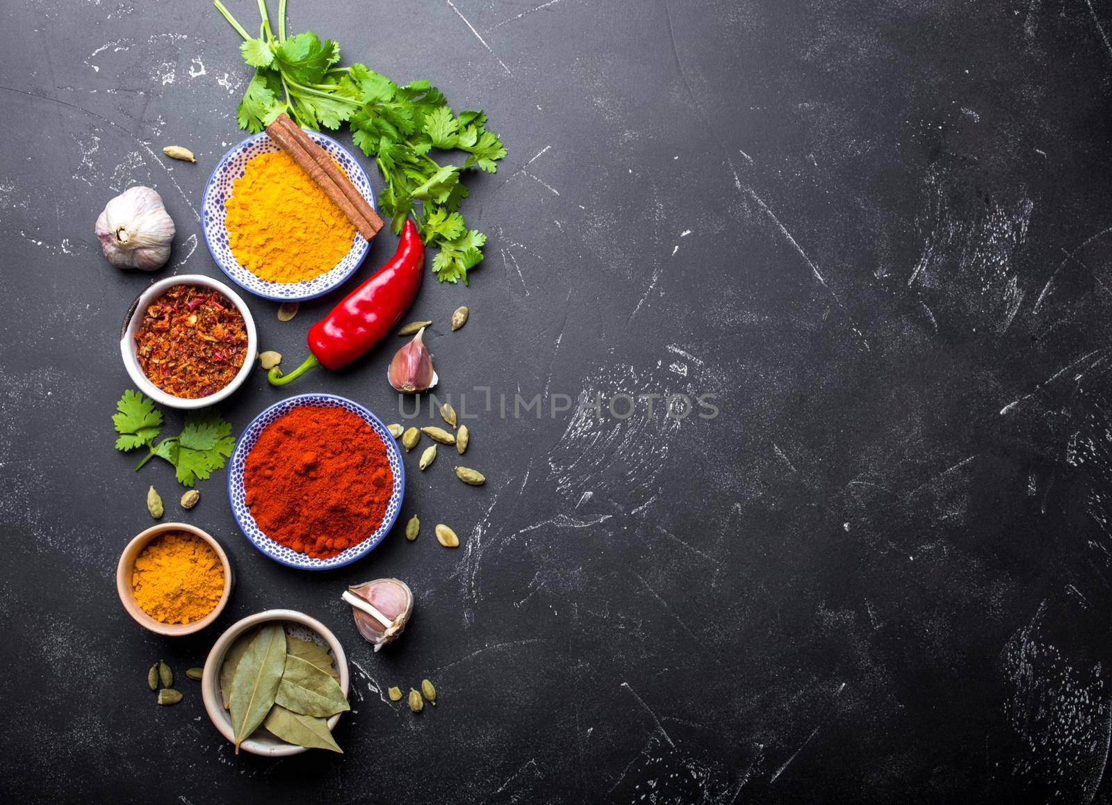 Indian food cooking background. Traditional Indian spices and ingredients. Curry, turmeric, cardamom, garlic, pepper, fresh cilantro, cinnamon. Preparing exotic meal. Top view, space for text