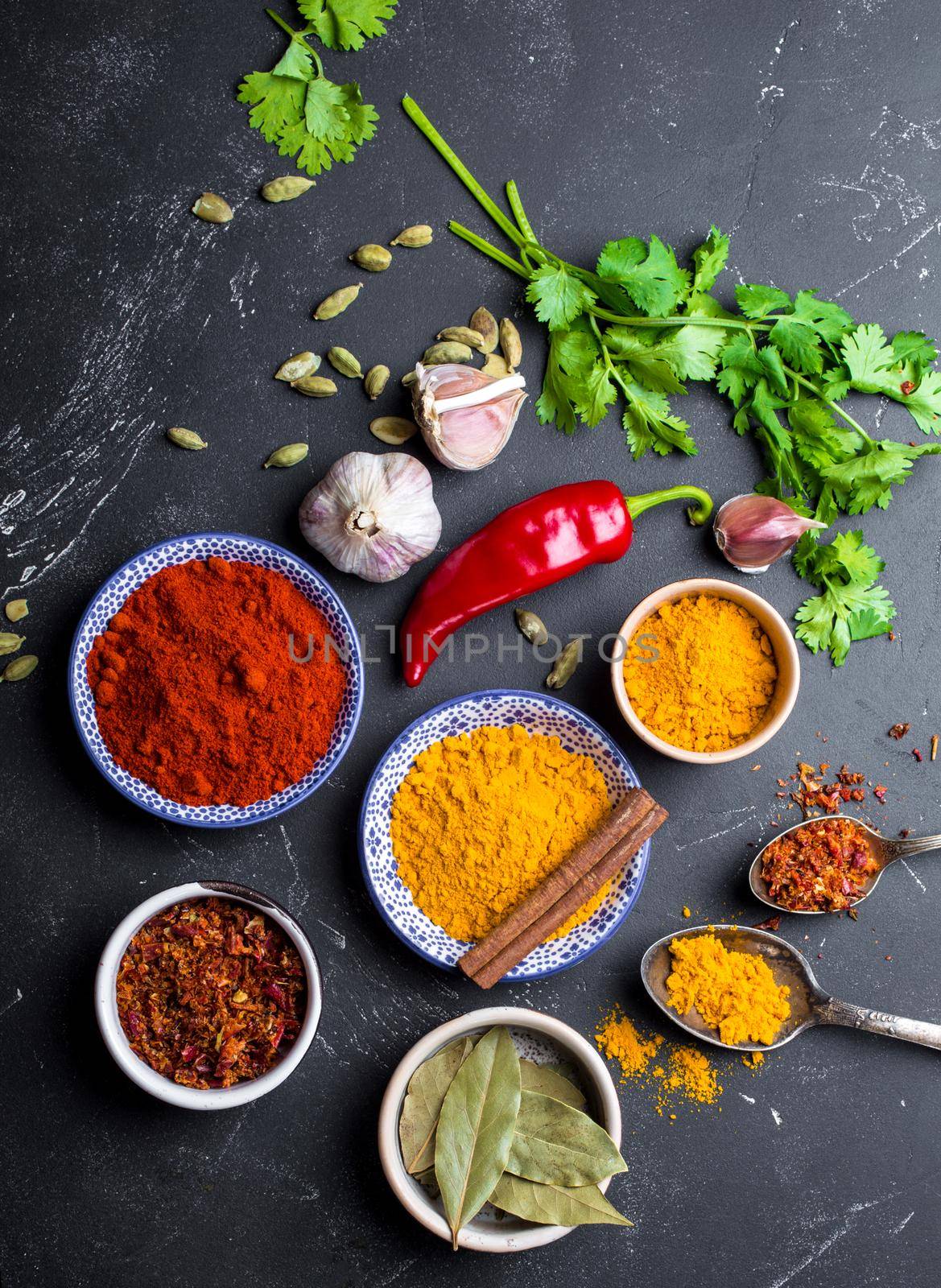 Set of Indian food cooking ingredients. Traditional Indian assorted spices and herbs. Curry, turmeric, cardamom, garlic, pepper, cilantro, cinnamon. Preparing exotic meal. Top view, close up