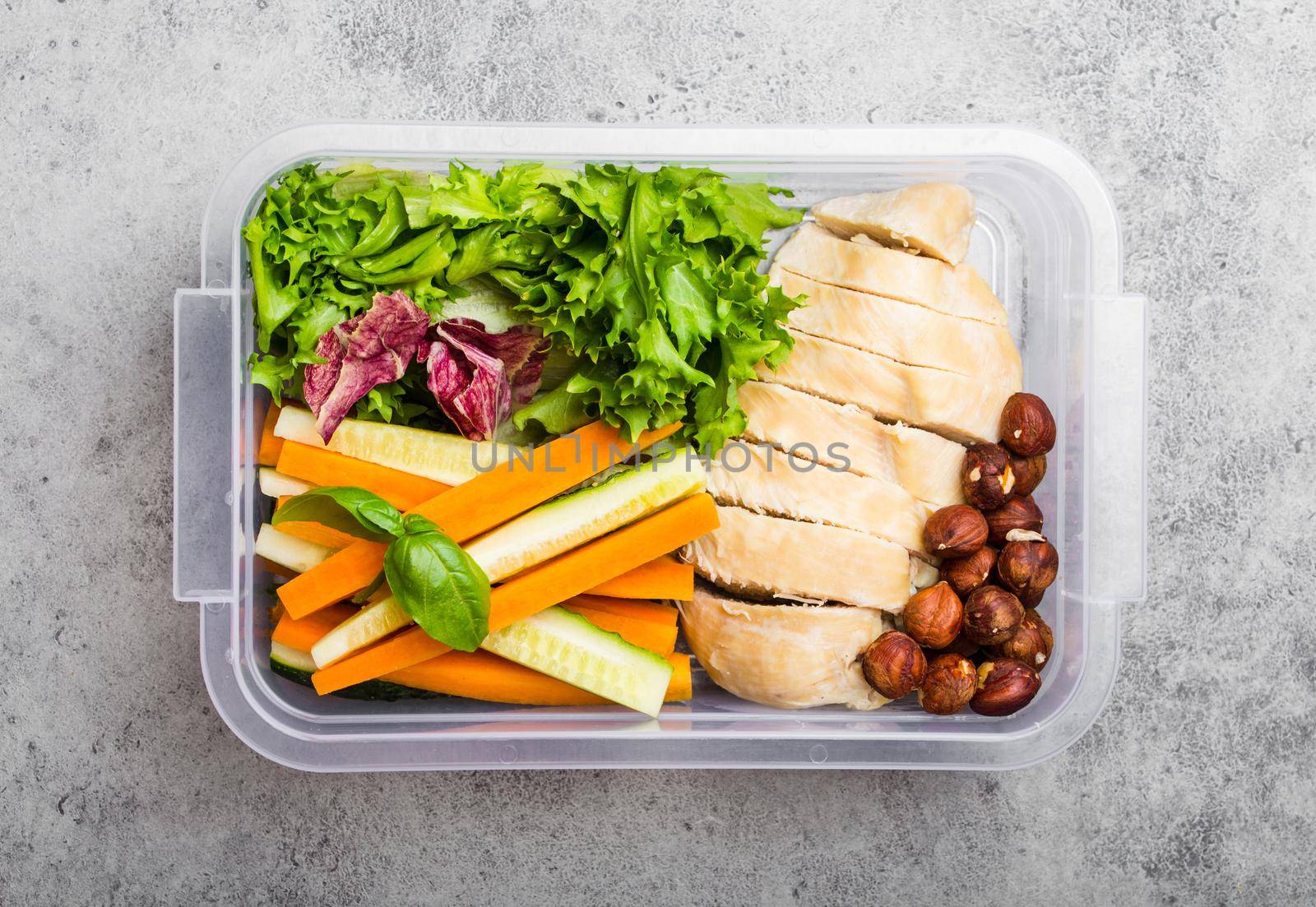 A lunch box for office or school with healthy food: chicken fillet, carrot and cucumber sticks, salad, nuts. Preparation and packaging of meal made in advance to support a balanced lifestyle or diet