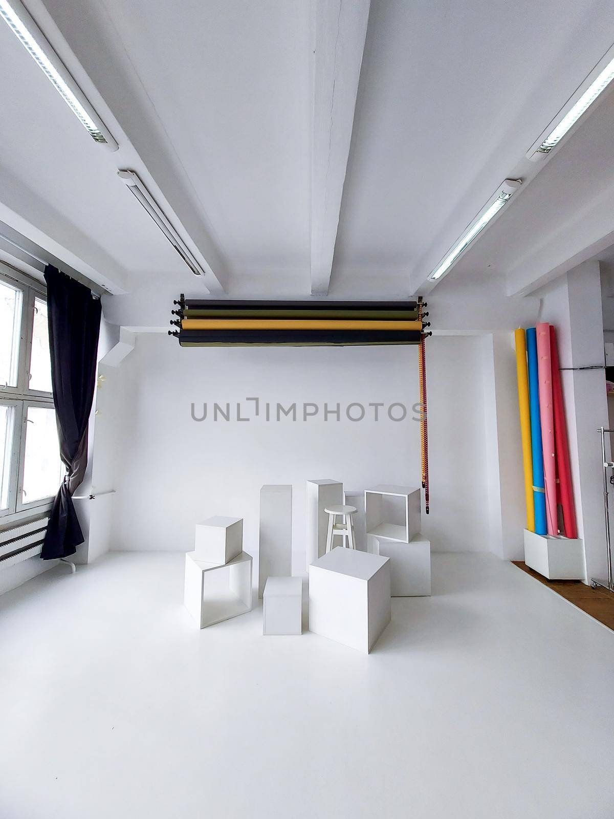 Daylight photo studio interior with set of professional equipment as a rolls of color background and white cubes on a white floor. by vovsht