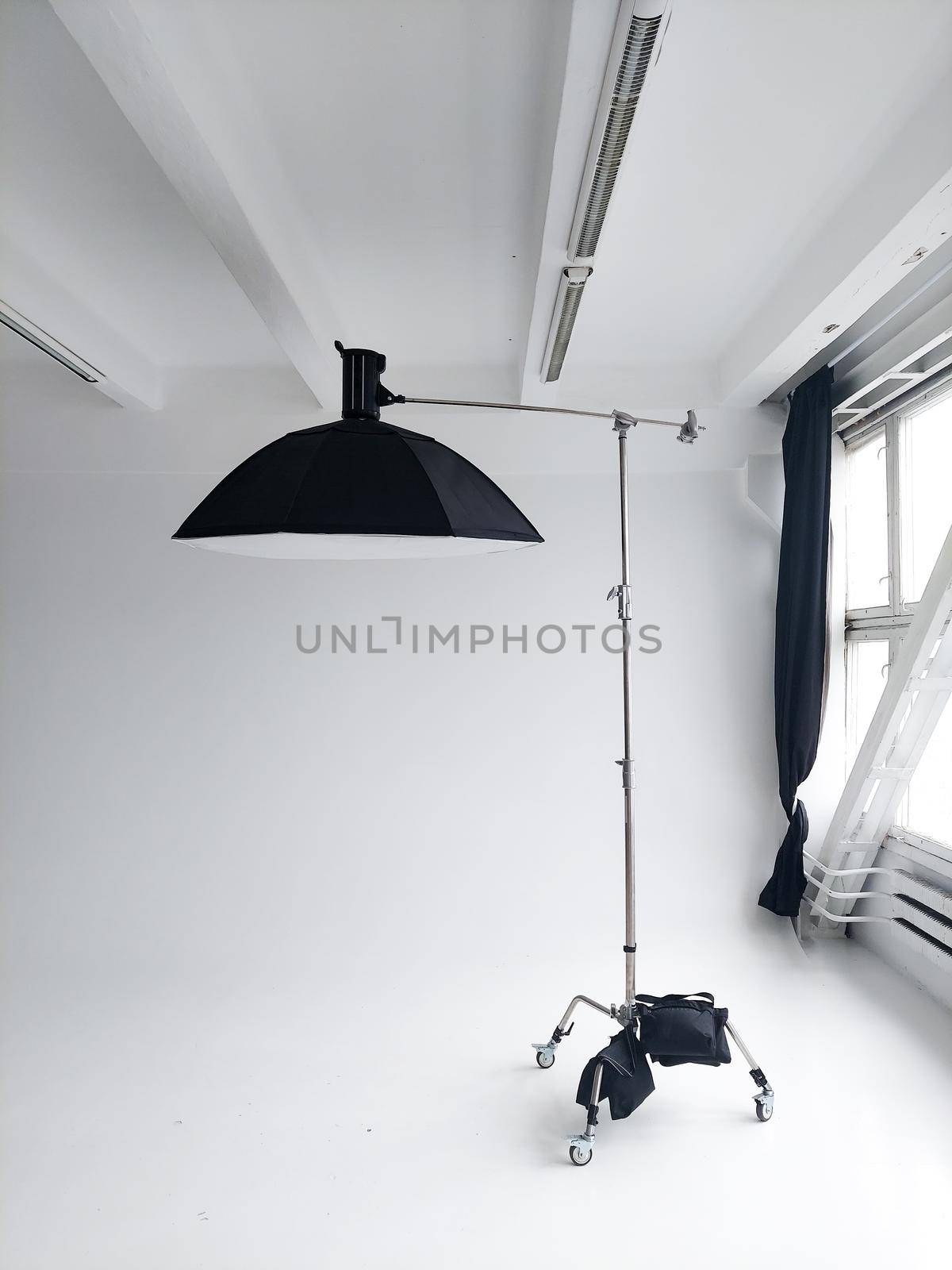 Professional photo flash light with a big softbox on a c-stand on a cyclorama in modern photo studio with a huge windows. Professional lighting equipment, flashes, c-stands. by vovsht
