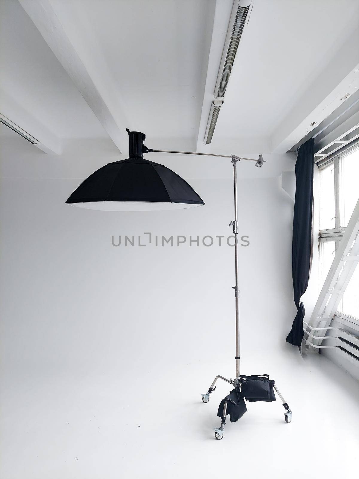 Professional photo flash light with a big softbox on a c-stand on a cyclorama in modern photo studio with a huge windows. Professional lighting equipment, flashes, c-stands