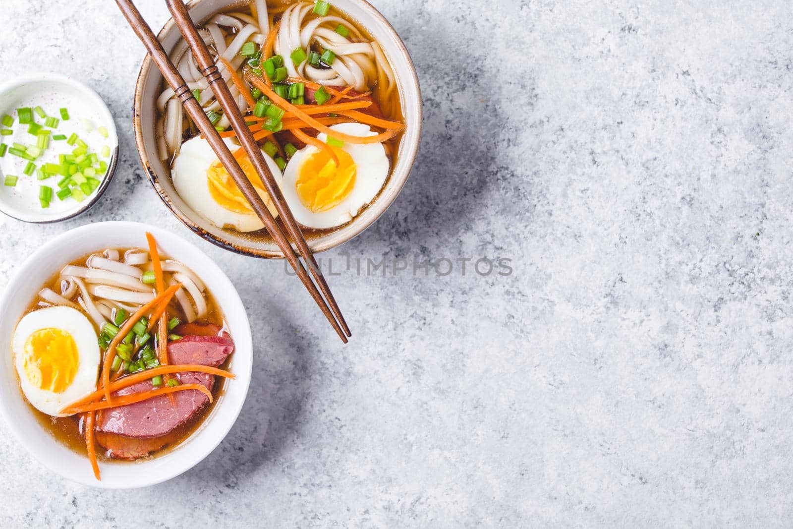 Bowls with Japanese soup ramen, chopsticks, white concrete rustic background. Traditional Asian soup with noodles, meat, eggs. Asian food. Japanese ramen for dinner. Ramen, close-up. Space for text.