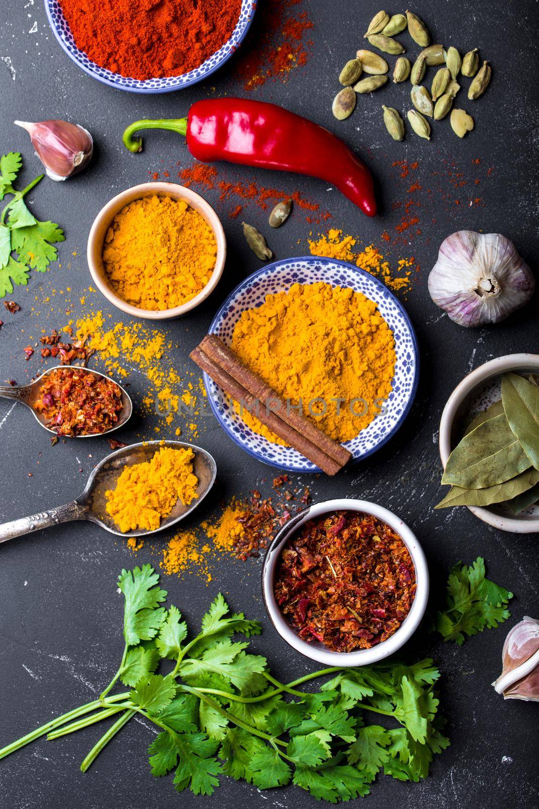 Set of Indian food cooking ingredients. Traditional Indian assorted spices and herbs. Curry, turmeric, cardamom, garlic, pepper, cilantro, cinnamon. Preparing exotic meal. Top view, close up