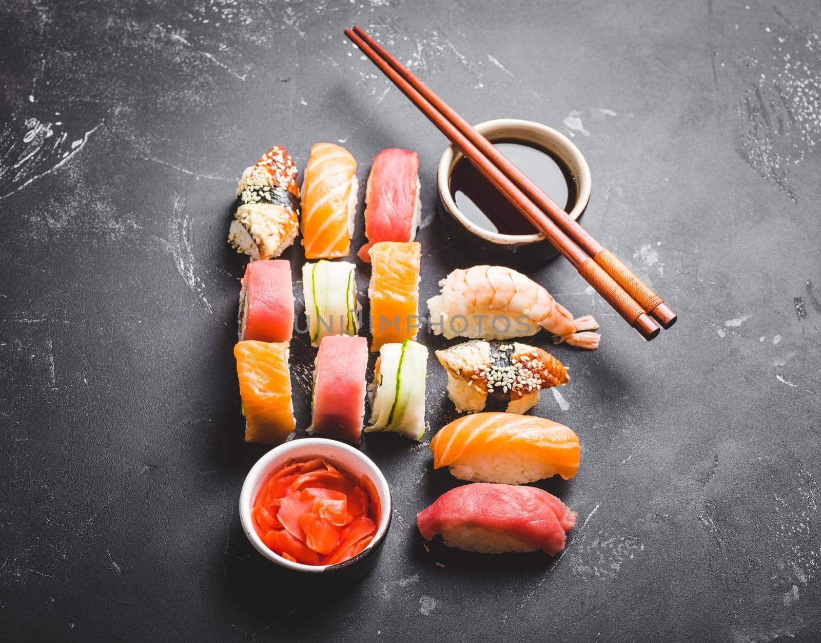 Top view of assorted mixed Japanese sushi set with rolls, nigiri, soy sauce, ginger, chopsticks on black concrete background. Asian dinner or lunch concept.