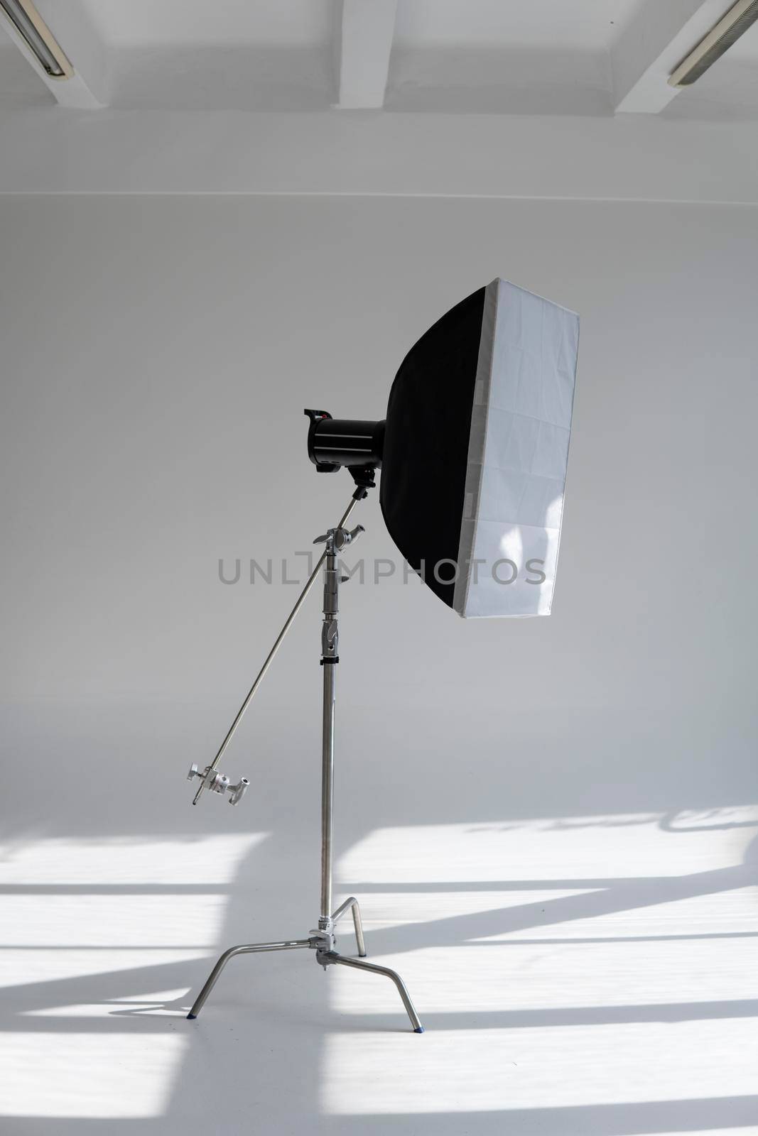 Professional photo flash light with a big softbox on a c-stand on a cyclorama in modern photo studio with a huge windows. Professional lighting equipment, flashes, c-stands