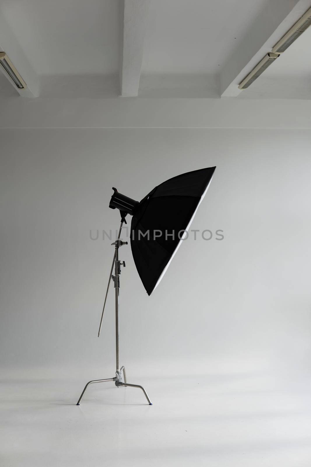 Professional photo flash light with a big softbox on a c-stand on a cyclorama in modern photo studio with a huge windows. Professional lighting equipment, flashes, c-stands. by vovsht