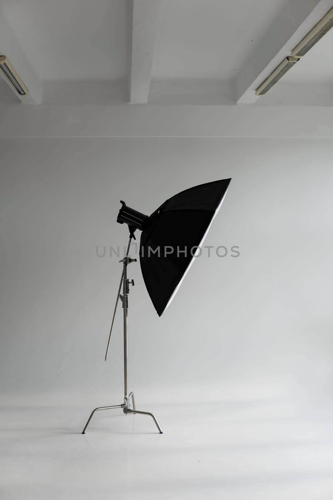 Professional photo flash light with a big softbox on a c-stand on a cyclorama in modern photo studio with a huge windows. Professional lighting equipment, flashes, c-stands