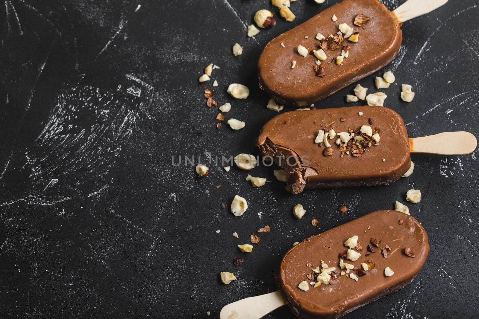 Milk chocolate popsicles with hazelnuts. Close-up. Ice cream popsicles covered with chocolate, sticks, black stone marble background. Space for text. Top view. Chocolate ice cream bars, nuts. Dessert