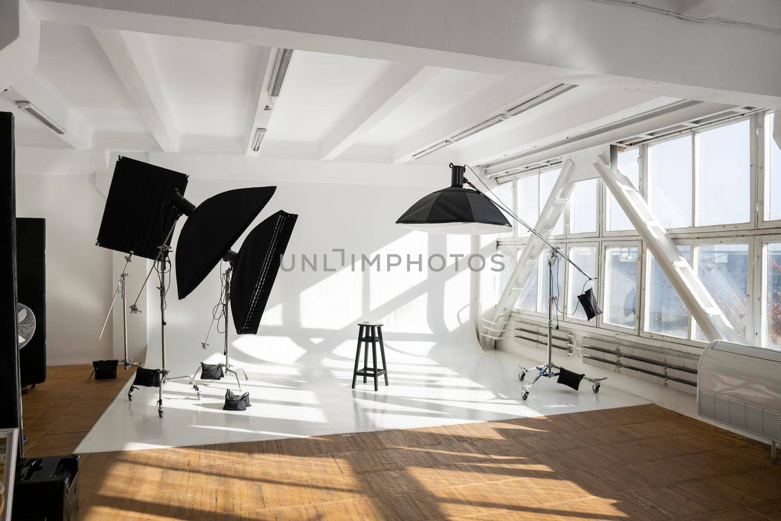 Professional lighting equipment, flashes, c-stands on a cyclorama in modern photo studio with a huge windows. Octabox, stripbox, softbox, buety plate and other stuff for photography. by vovsht