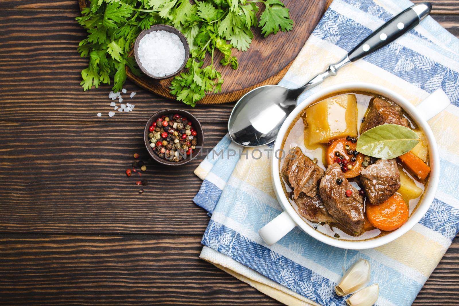 Close-up of slow cooked meat stew ragout in bowl with beef, potato, carrot, broth on wooden rustic background, top view with space for text. Hot homemade food for dinner, meat casserole copy space.