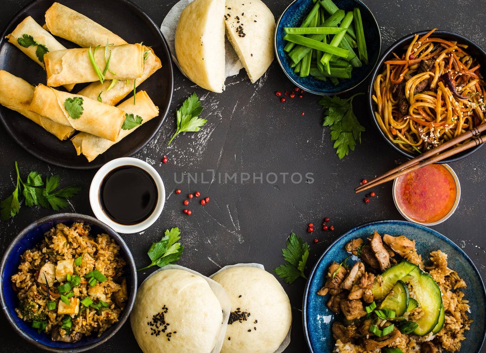 Asian assorted food set, dark rustic stone background. Chinese dishes. Chinese stir-fry noodles, asian rice with meat, dim sum, fried spring rolls, steamed Chinese buns. Space for text. Top view