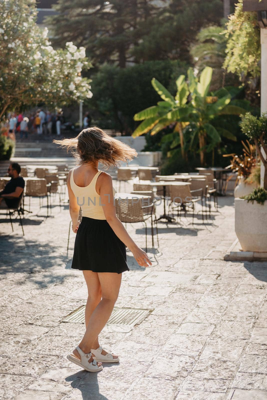 Girl tourist walking through ancient narrow street on a beautiful summer day in MEDITERRANEAN MEDIEVAL CITY , OLD TOWN bUDVA, MONTENEGRO. Young beautiful cheerful woman walking on old street at tropical town. Pretty girl looking at you and smiling