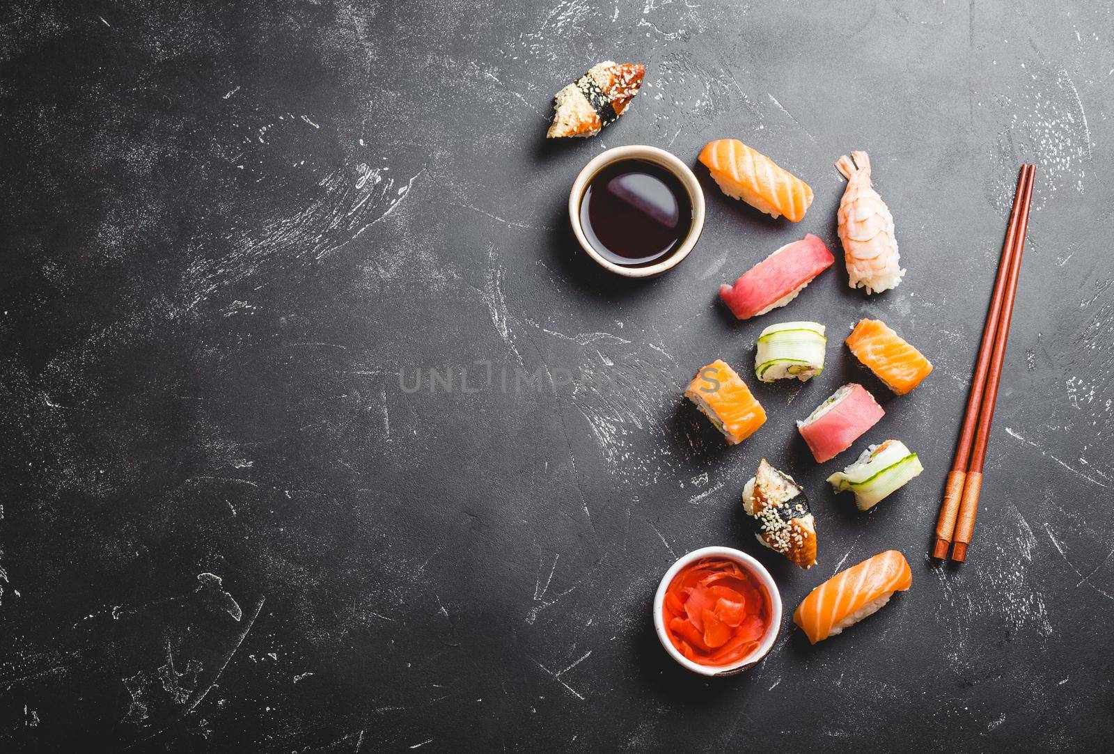 Top view of assorted mixed Japanese sushi set with rolls, nigiri, soy sauce, ginger, chopsticks on black concrete background with free space for text. Asian dinner or lunch .