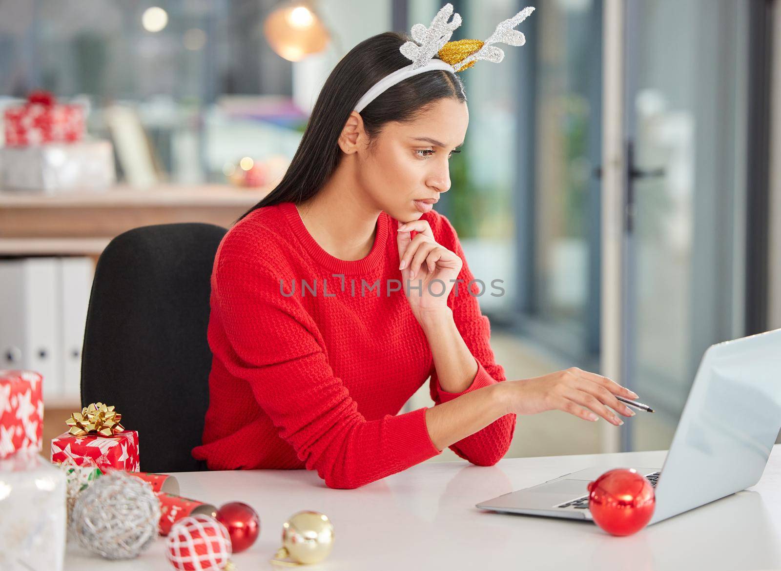 Finish up then the festivities can begin. a young businesswoman using a laptop in a modern office at Christmas