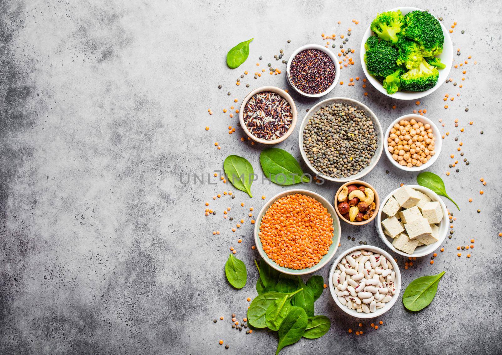 Top view of different vegan protein sources with space for text: beans, lentils, quinoa, tofu, vegetables, nuts, chickpeas, rice, stone background. Healthy balanced vegetarian nutrition for vegans