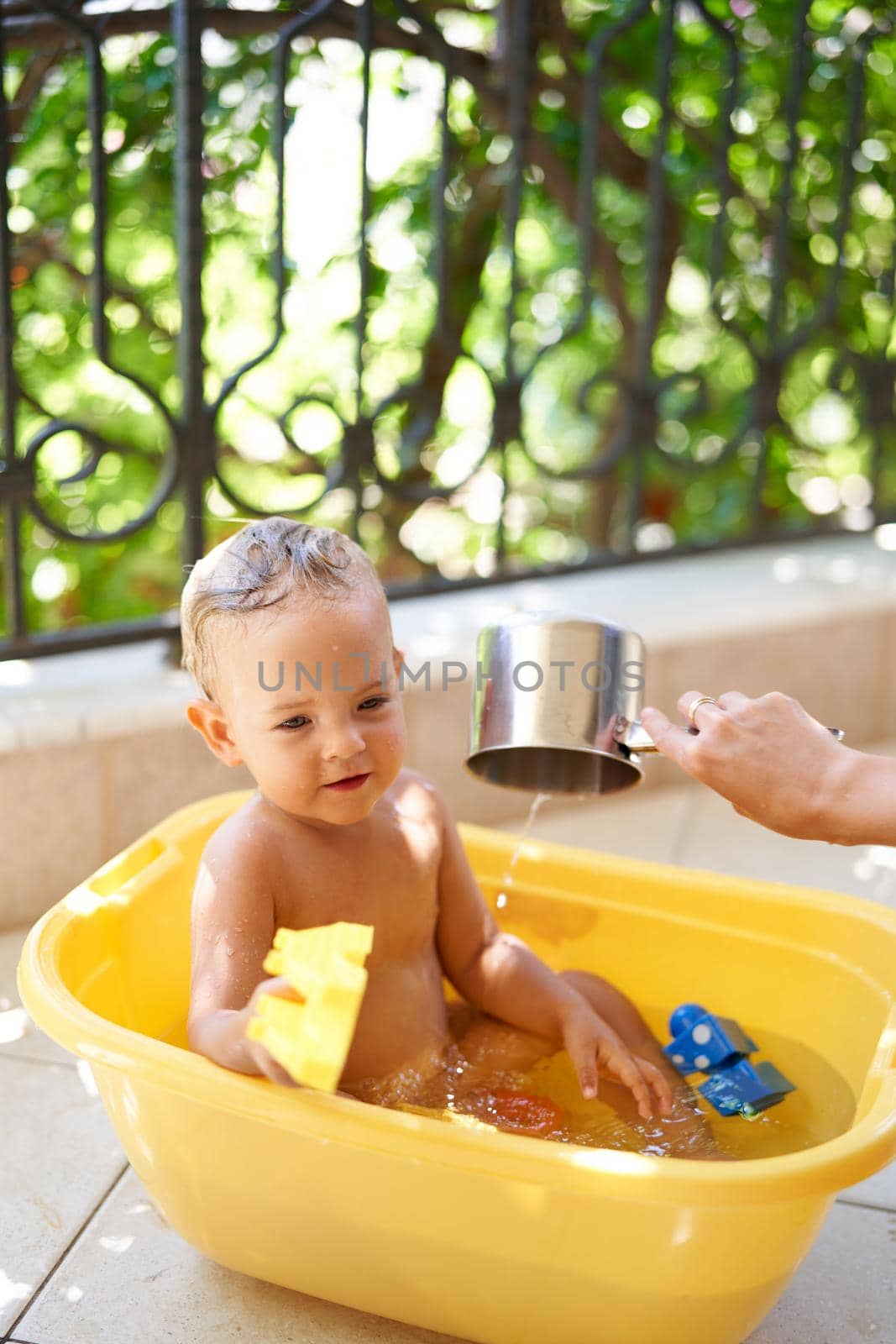 Little girl sitting in a bowl of water with a toy in her hand. High quality photo