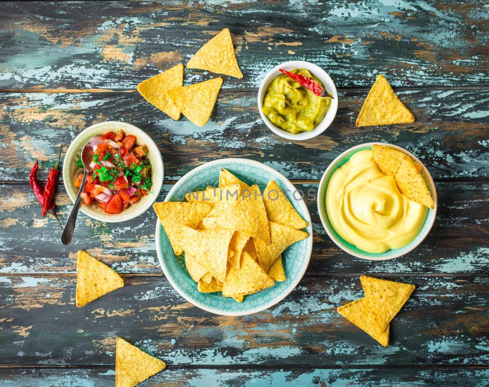 Mexican tortilla chips with guacamole, cheese, salsa dips. Nachos and assorted dips. Mexican party food, appetizers. Top view. Tortilla chips, sauces, hot pepper, avocado, rustic wooden background