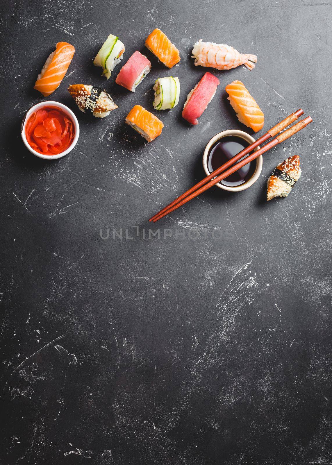 Top view of assorted mixed Japanese sushi set with rolls, nigiri, soy sauce, ginger, chopsticks on black concrete background with free space for text. Asian dinner or lunch .