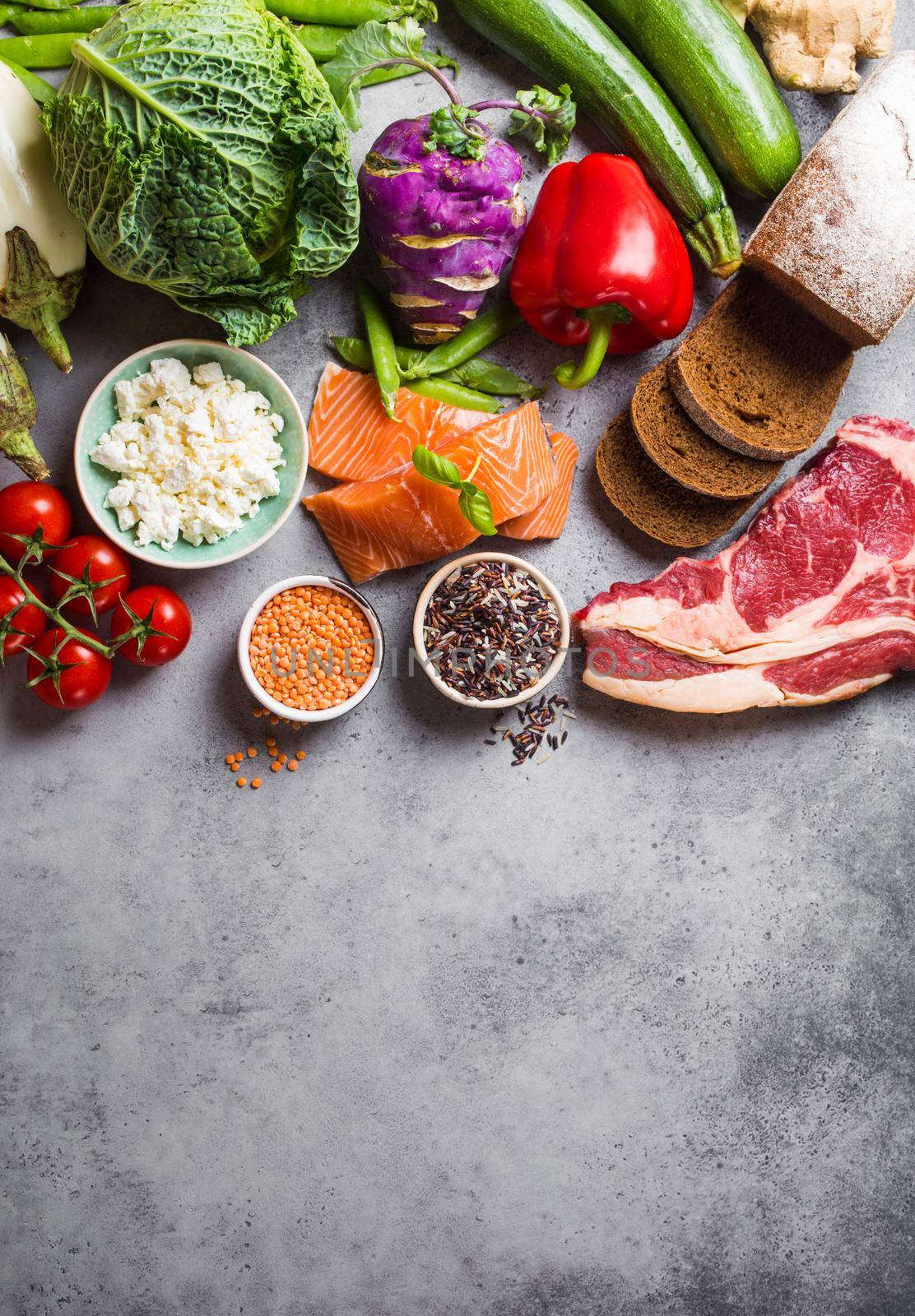 Top view of assortment of healthy balanced food: meat, fish, vegetables, bread, cereals, beans, stone background, space for text. Raw ingredients for cooking healthy meal, good for diet, clean eating