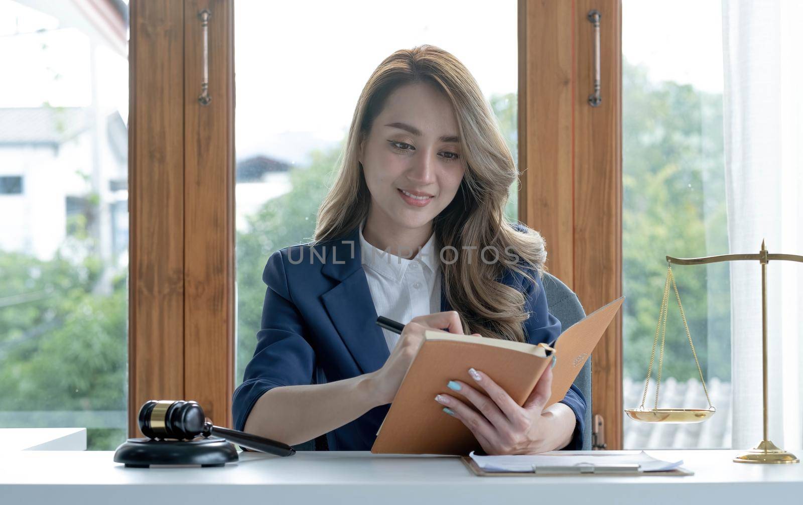 Confident and successful young Asian female lawyer or business legal consultant reading a law book or writing something on her notebook at her office