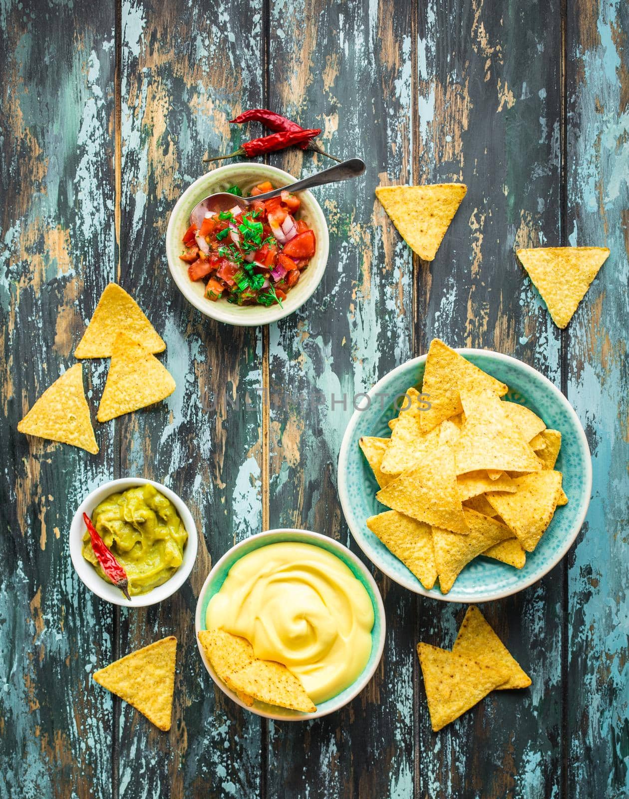 Mexican tortilla chips with guacamole, cheese, salsa dips. Nachos and assorted dips. Mexican party food, appetizers. Top view. Tortilla chips, sauces, hot pepper, avocado, rustic wooden background