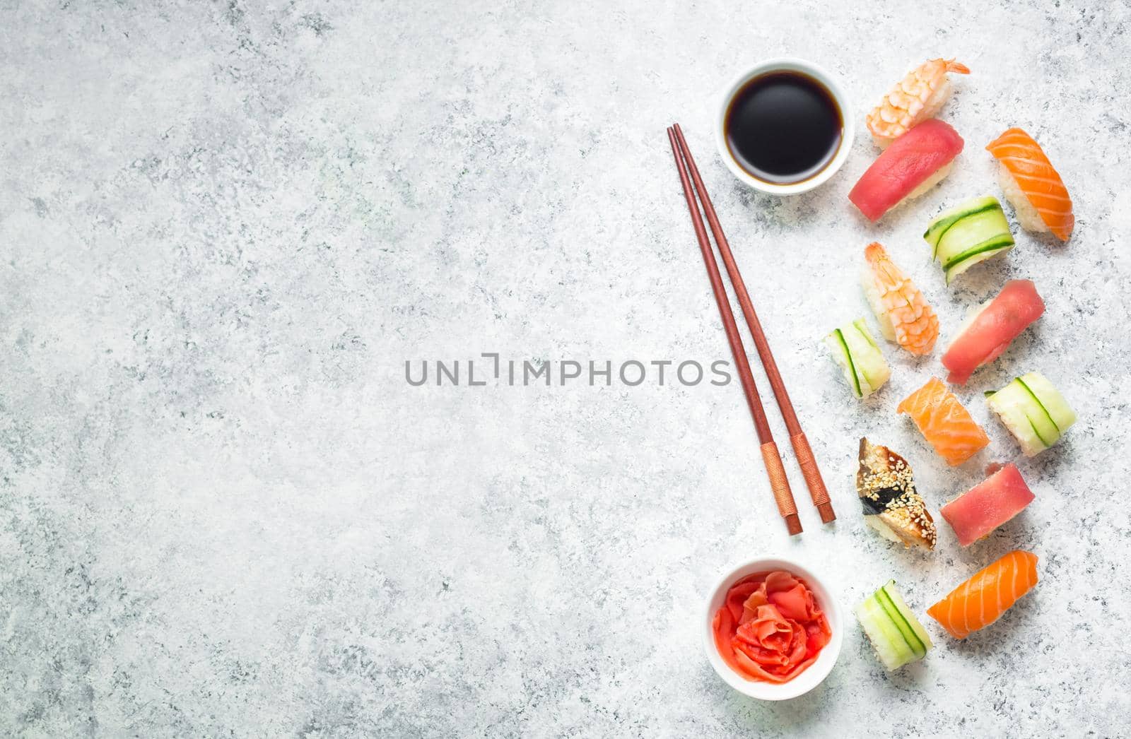 Assorted sushi set on white concrete background. Space for text. Japanese sushi, rolls, soy sauce, ginger, chopsticks. Top view. Sushi nigiri. Japanese dinner/lunch. Food frame. Different sushi mixed