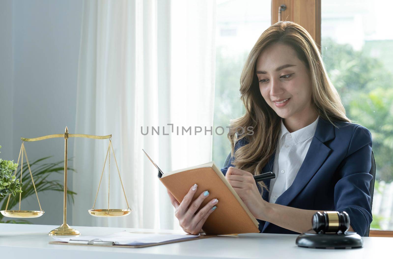 Confident and successful young Asian female lawyer or business legal consultant reading a law book or writing something on her notebook at her office