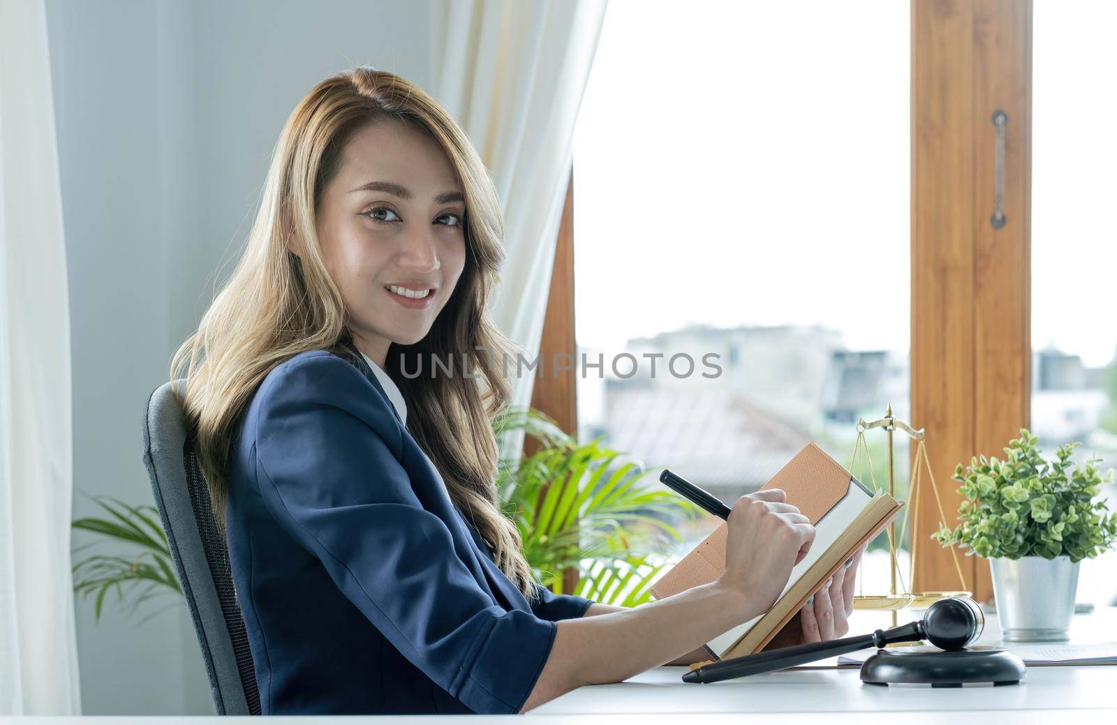 Confident and successful young Asian female lawyer or business legal consultant reading a law book or writing something on her notebook at her office