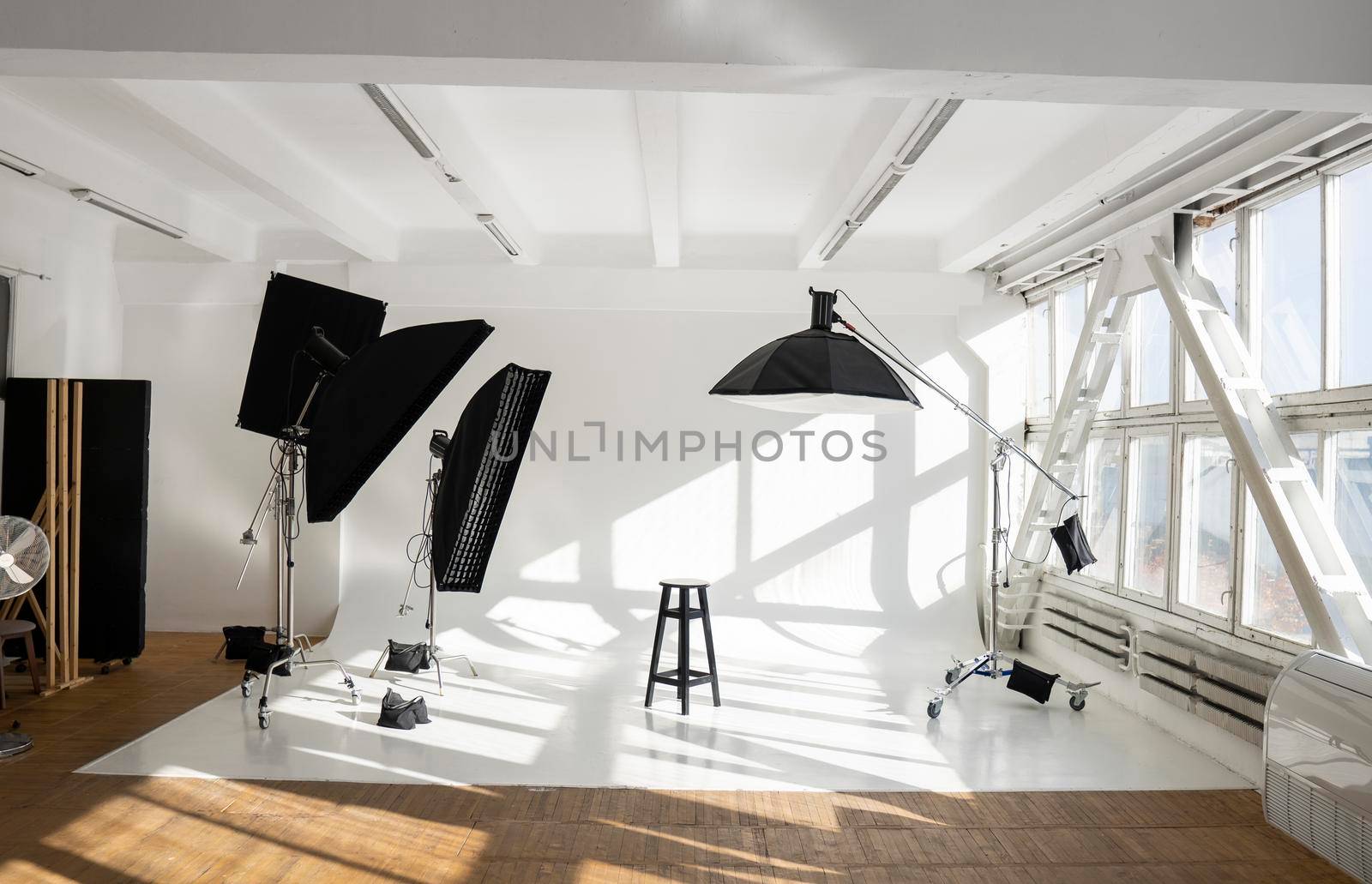 Professional lighting equipment, flashes, c-stands on a cyclorama in modern photo studio with a huge windows. Octabox, stripbox, softbox, buety plate and other stuff for photography. by vovsht