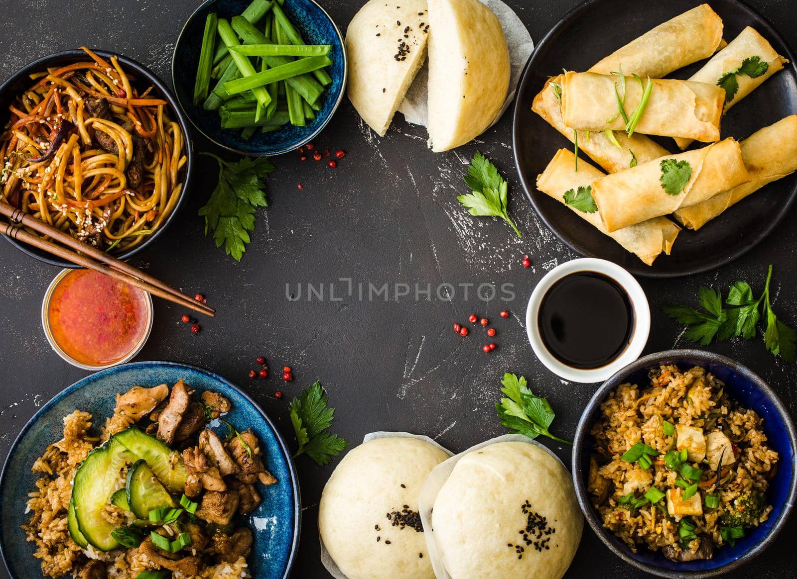 Asian assorted food set, dark rustic stone background. Chinese dishes. Chinese stir-fry noodles, asian rice with meat, dim sum, fried spring rolls, steamed Chinese buns. Space for text. Top view