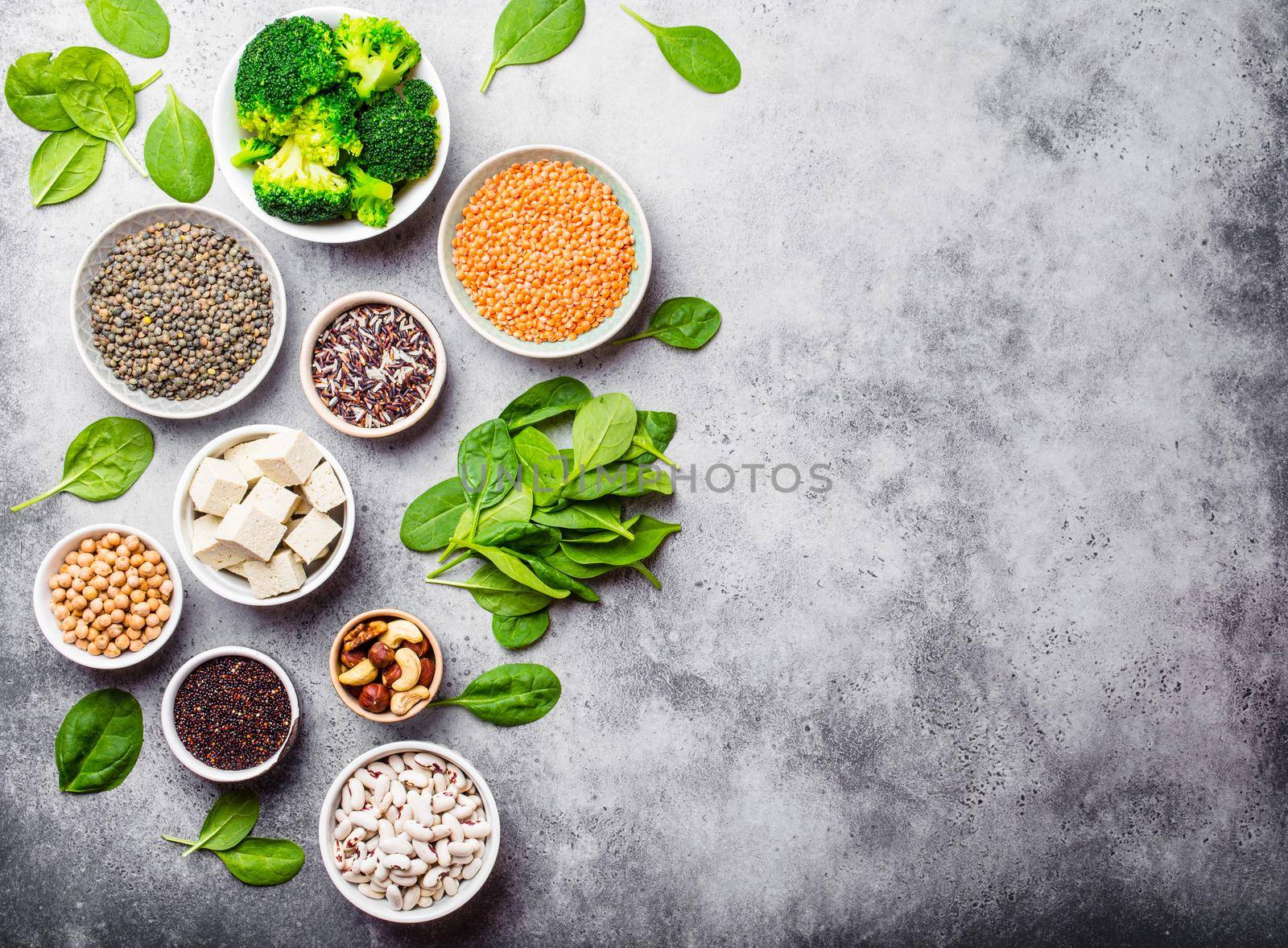 Top view of different vegan protein sources with space for text: beans, lentils, quinoa, tofu, vegetables, nuts, chickpeas, rice, stone background. Healthy balanced vegetarian nutrition for vegans