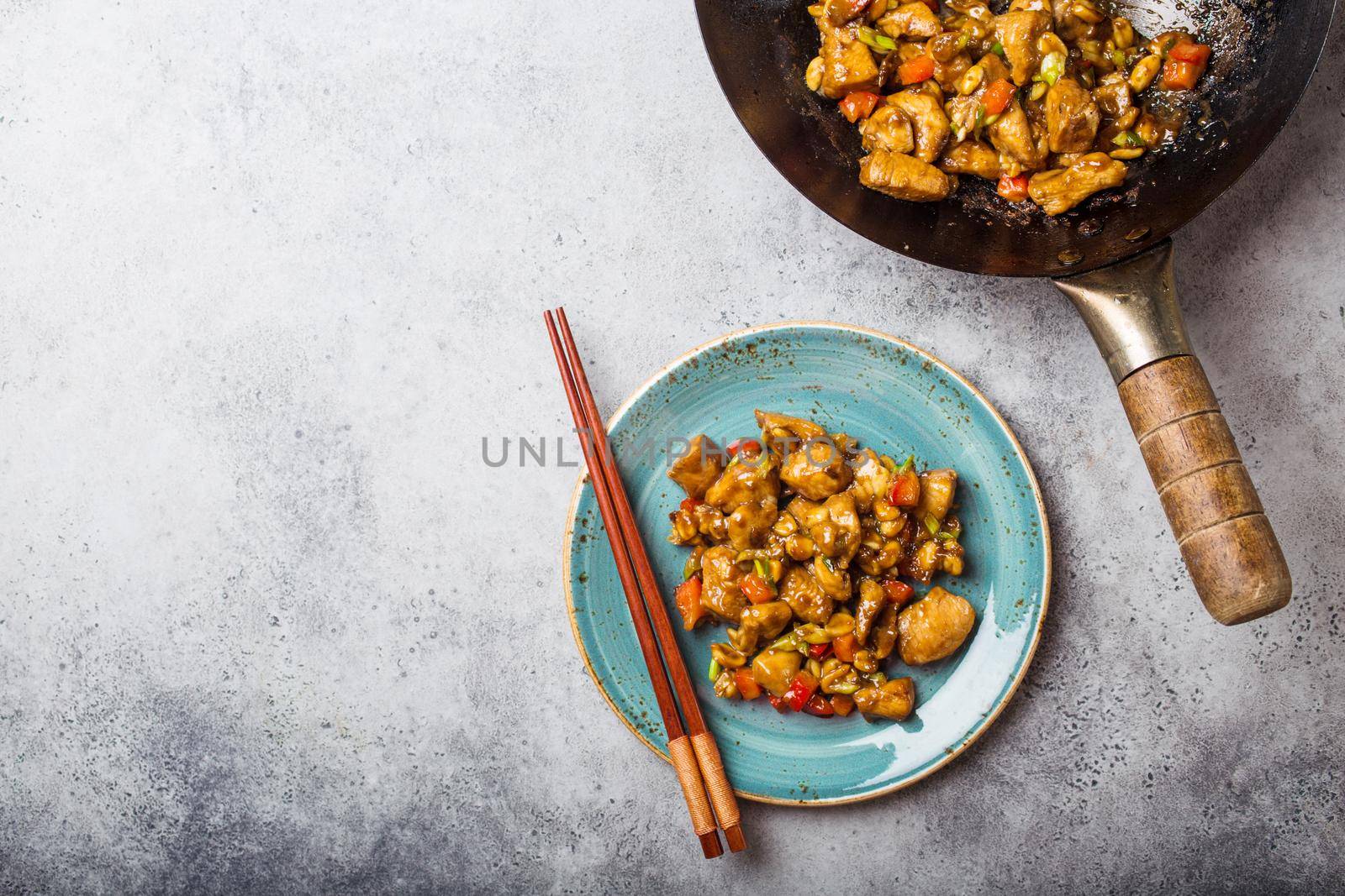 Top view of Kung Pao chicken on plate ready for eat, space for text. Stir-fried Chinese traditional dish with chicken, peanuts, vegetables, chili peppers. Chinese dinner, chopsticks, stone background