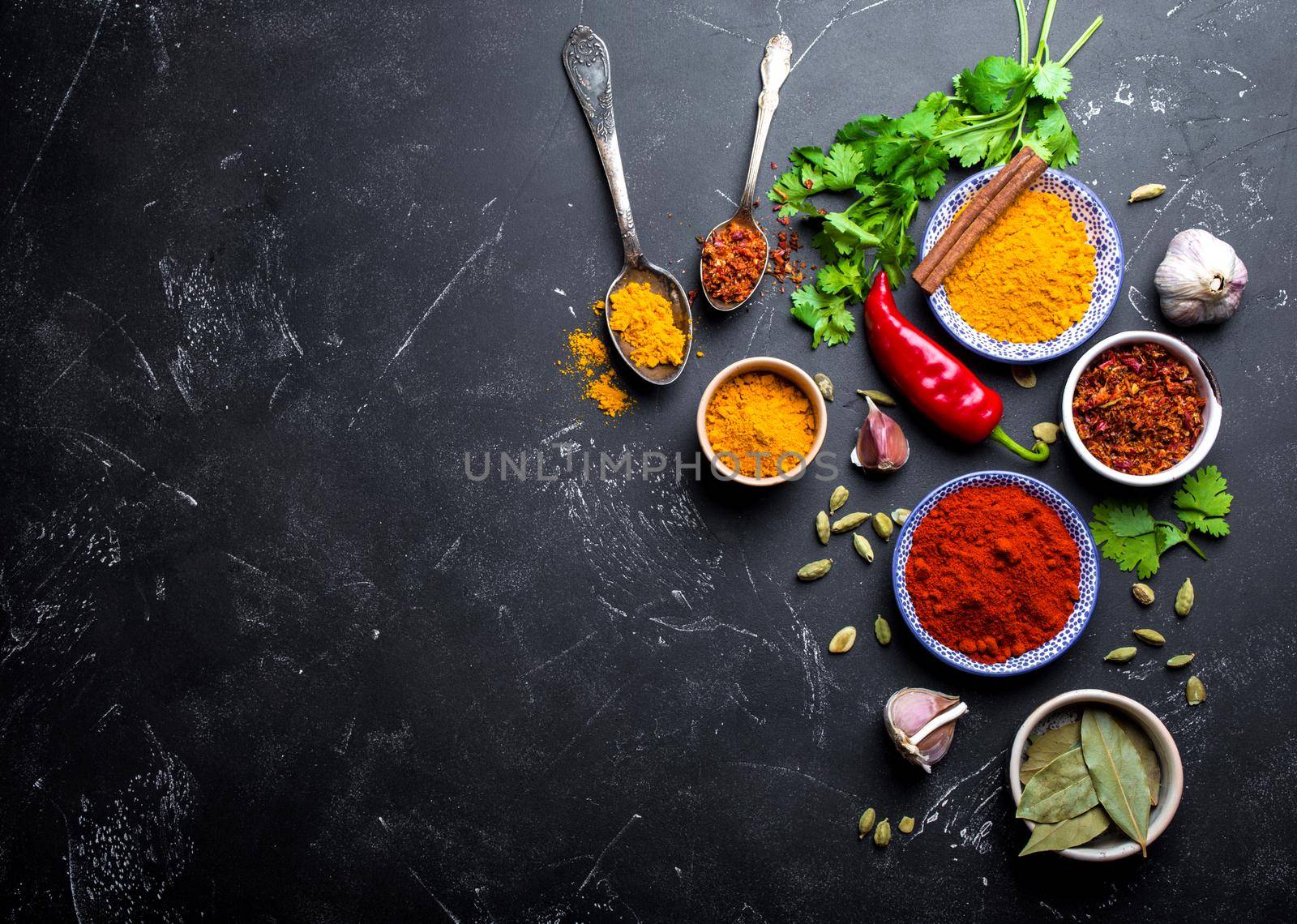 Indian food cooking background. Traditional Indian spices and ingredients. Curry, turmeric, cardamom, garlic, pepper, fresh cilantro, cinnamon. Preparing exotic meal. Top view, space for text