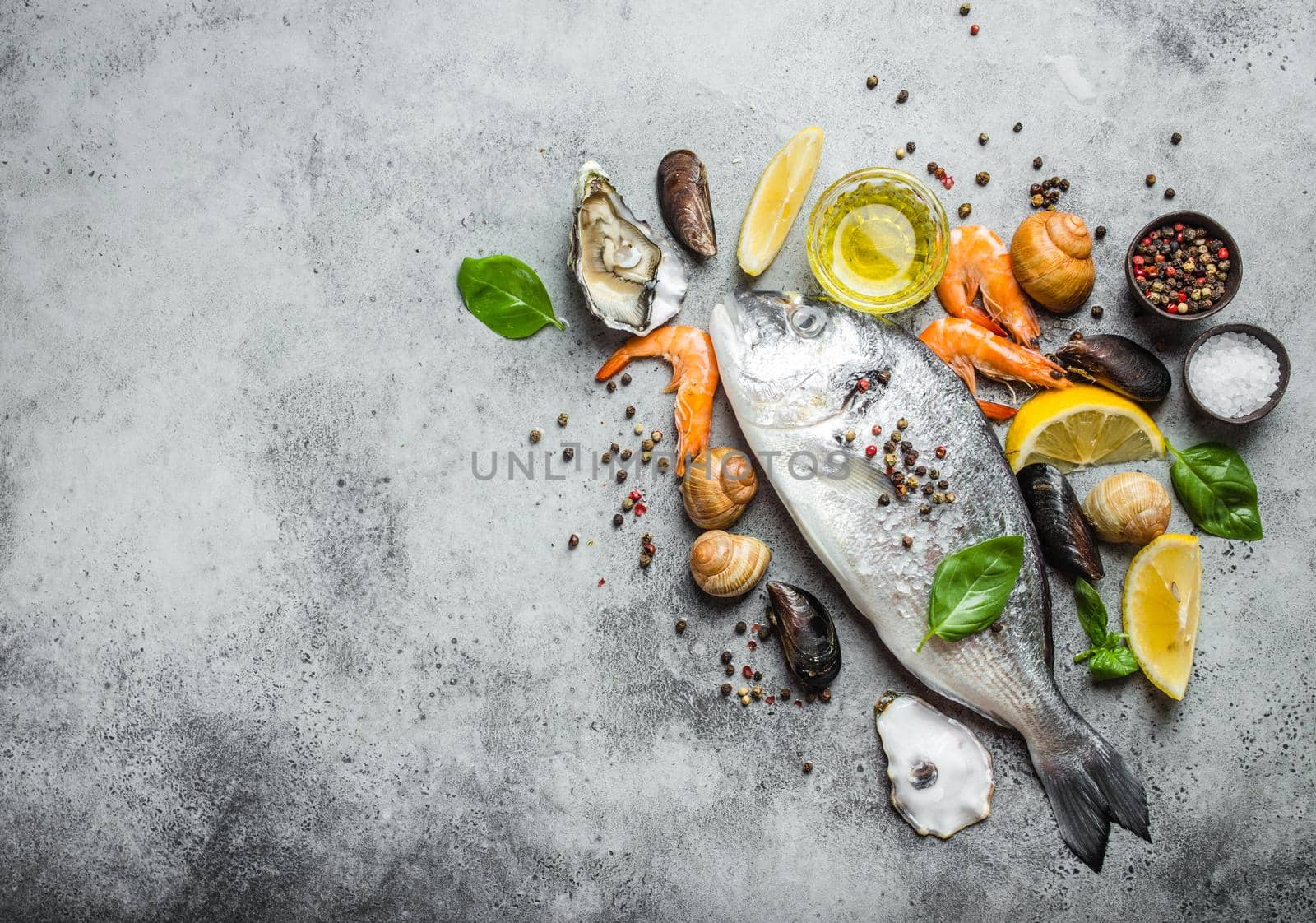 Fresh raw fish Dorado, oysters, shrimps, clams, mussels, shells with lemon, olive oil, herbs on grey stone rustic background, top view, space for text. Cooking fish and seafood, copy space