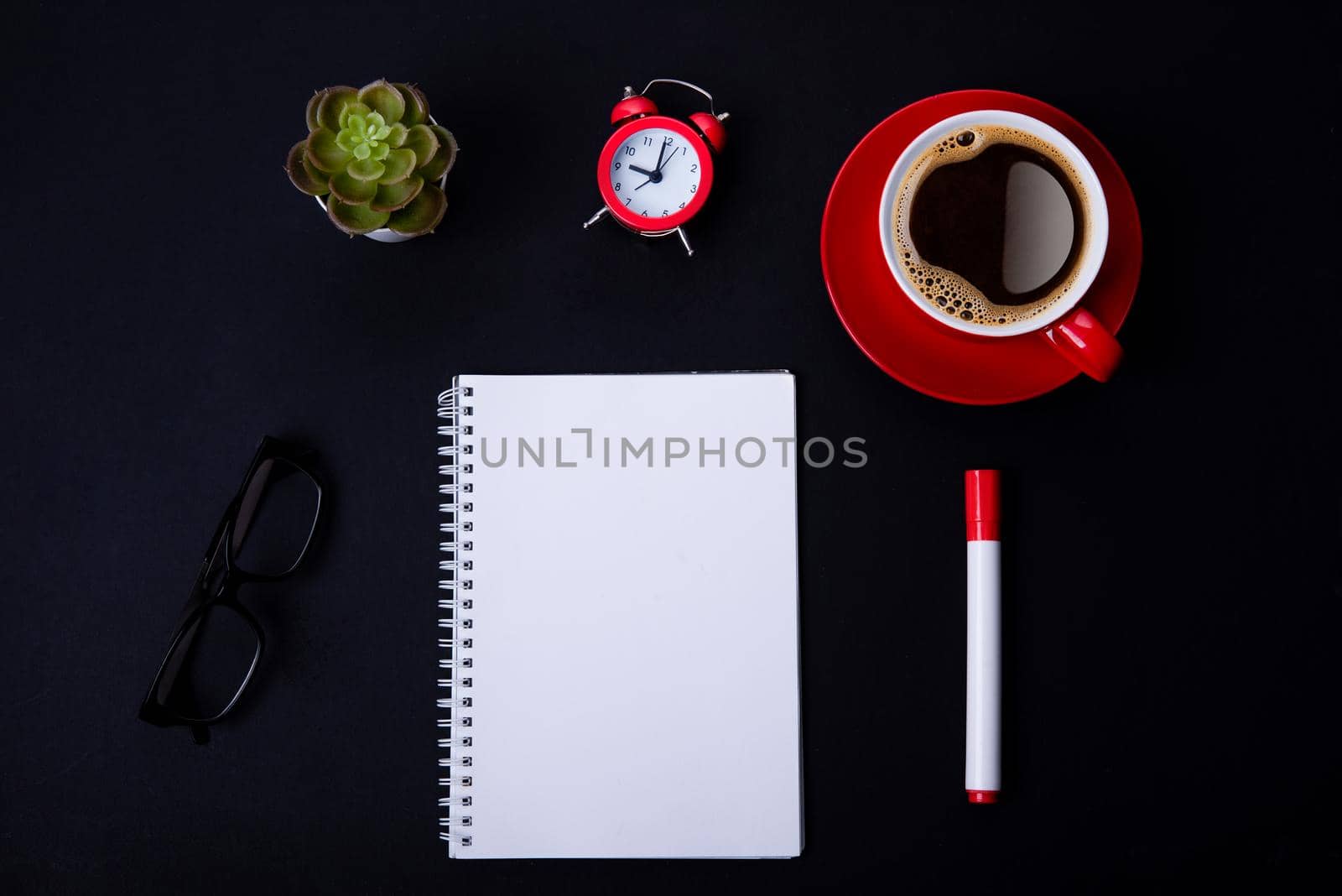 red cup of coffee, pen, glasses, alarm, plant, phone, and paper on a black background as workplace top view space for text by Iryna_Melnyk